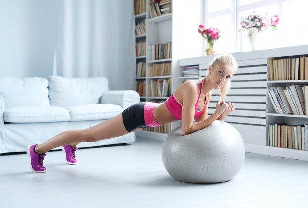Fitness blonde woman doing stretches with her exercise ball at home