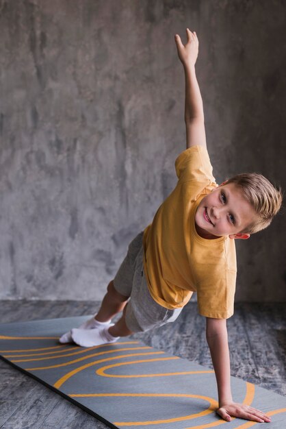 Fitness boy exercising on exercise mat in front of concrete wall