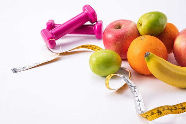 Fitness composition with pink dumbbells, fresh fruits, and measuring tape on a white surface