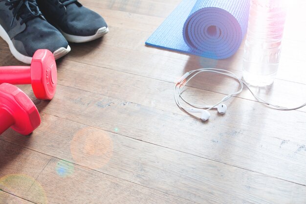 Fitness concept with bottle of water, sneakers, red dumbbells, yoga mat and earphones on wood floor, Copy space