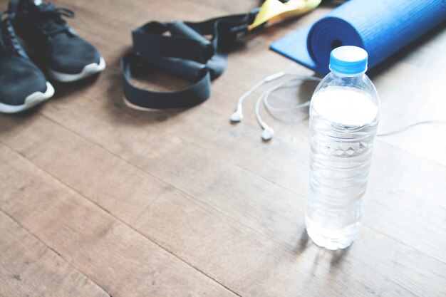 Fitness concept with bottle of water, sneakers, TRX, yoga mat and earphones on wood floor, Copy space