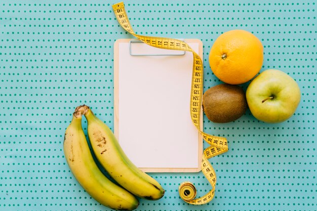 Fitness concept with clipboard, tape measure and healthy fruits