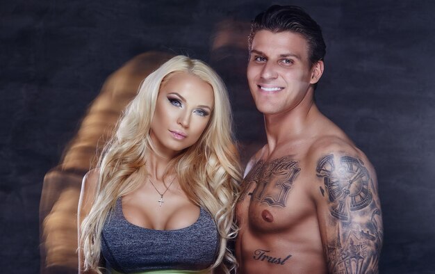 Fitness couple. Tattoed muscular man and blond woman posing in studio.
