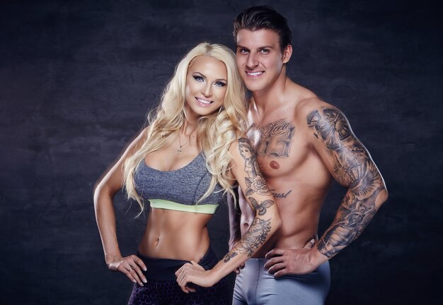 Fitness couple. Tattoed muscular man and blond woman posing in studio.