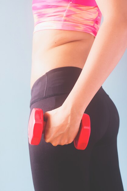 Fitness female in black pants and pink sport bra holding red dumbbell