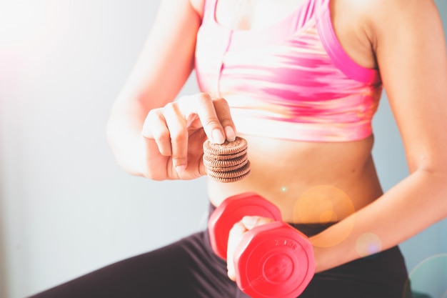 Fitness female in pink sport bra holding red dumbbell and snack in other hand with copy space