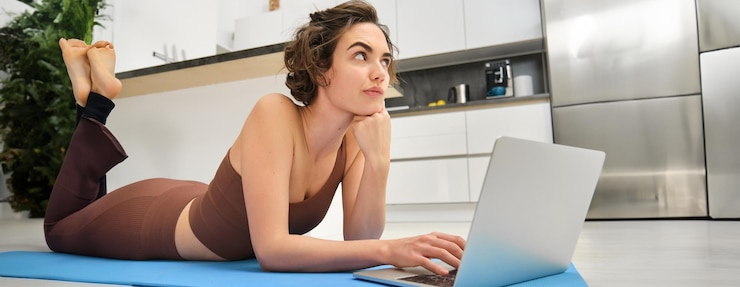 Free Photo fitness girl lying on rubber mat with thoughtful face using laptop fitness instructor thinking