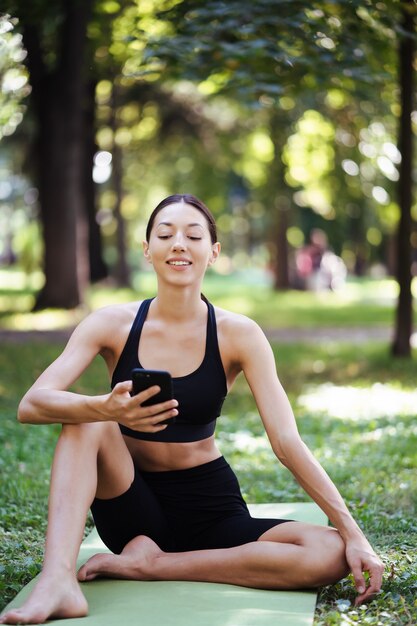Девушка фитнеса со смартфоном на фоне природы, любит спортивные тренировки. Женщина с помощью мобильного телефона на открытом воздухе.