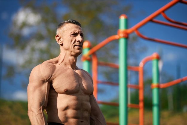 Fitness man with muscular bare torso posing on sports ground