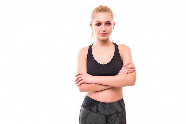 Fitness model with blonde hair is standing crossarmed in studio isolated on white