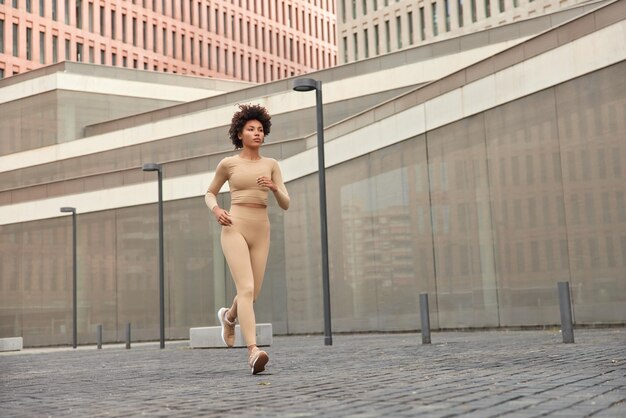 Fitness and running concept. Full length shot of active female runner dressed in active wears and sneakers jogs during morning in urban place