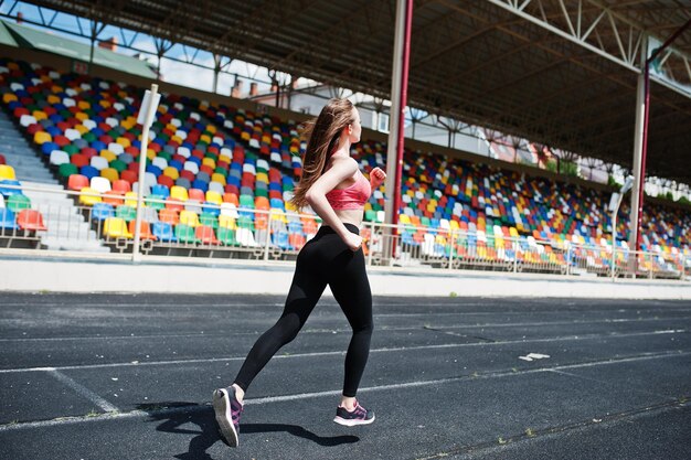 Фитнес-спортивная девушка в спортивной одежде на стадионе, спорт на открытом воздухе Счастливая сексуальная женщина, бегущая по беговой дорожке на стадионе
