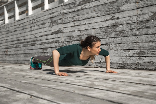 fitness sporty girl in sporty clothes is doing exercises on a wooden background, light background ,the concept of sports