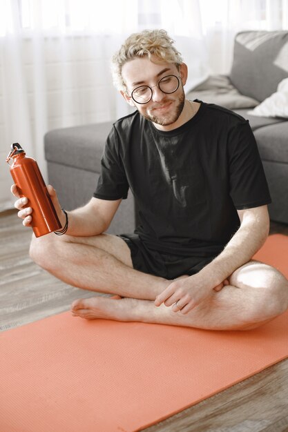 Fitness trainer or video blogger doing stretching. The man is filming himself on smartphone camera at home.