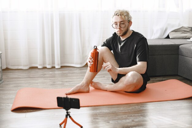 Fitness trainer or video blogger doing stretching. The man is filming himself on smartphone camera at home.