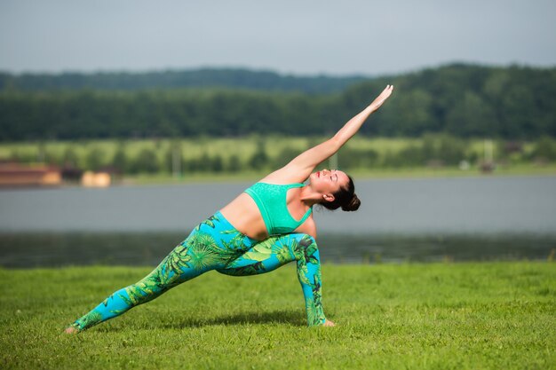 Женщина фитнеса делает упражнения йоги и расслабляется со спортивной одеждой в зеленом парке летом