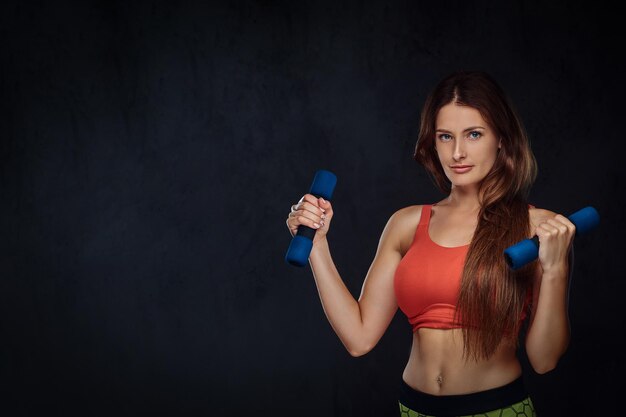 Fitness woman dressed in sports bra doing exercise with dumbbells. Isolated on a dark textured background.