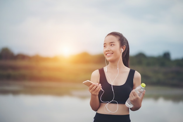 Женщина-фитнес в наушниках, слушая музыку во время тренировки и занятий в парке