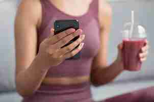 Free photo fitness woman having a detox juice while using a smartphone