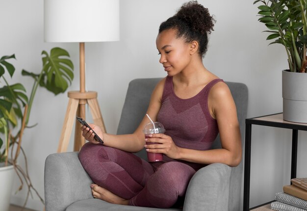 Fitness woman having a detox juice while using a smartphone