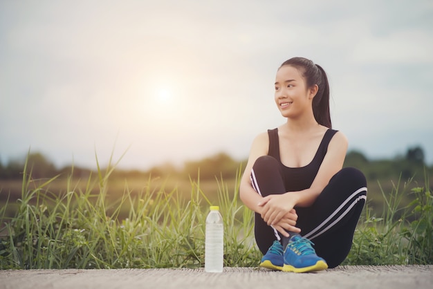 Free photo fitness woman runner sit down relaxing with water bottle after training outside in park