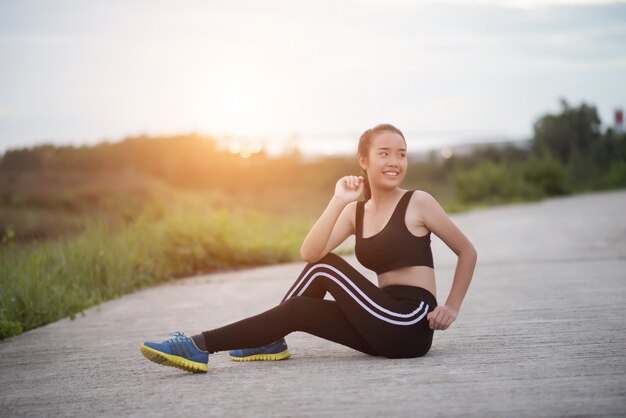  Fitness woman runner sit down relaxing with water bottle after training outside in park