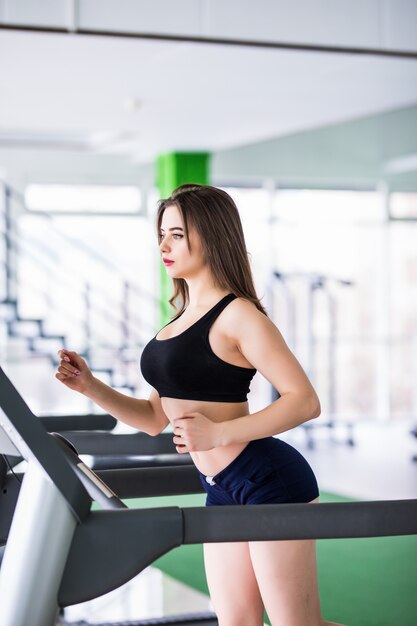 Fitness woman runs on sport simulator in modern fitness centre dressed up in black sportswear