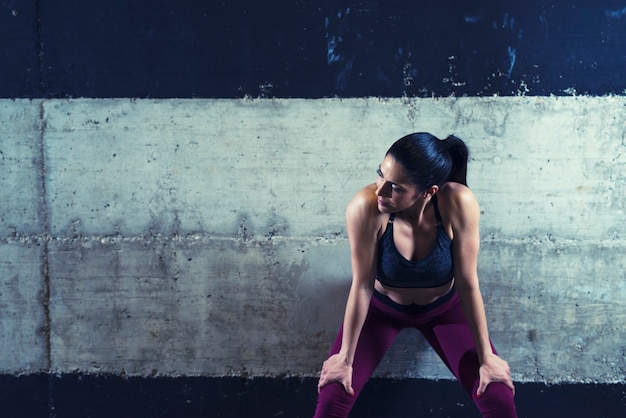 Donna di forma fisica in abiti sportivi che si appoggia sul muro di cemento e che osserva da parte