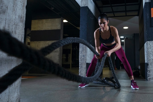 Fitness woman working out with battle ropes in the gym