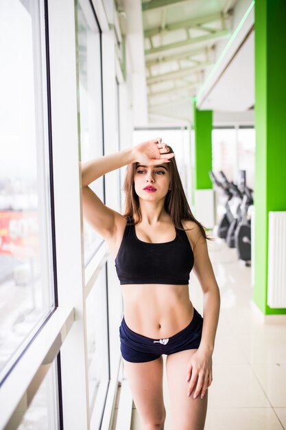 Fitness Young beauty with big green eyes strong fit body long brown hair is posing in gym in front of the windows