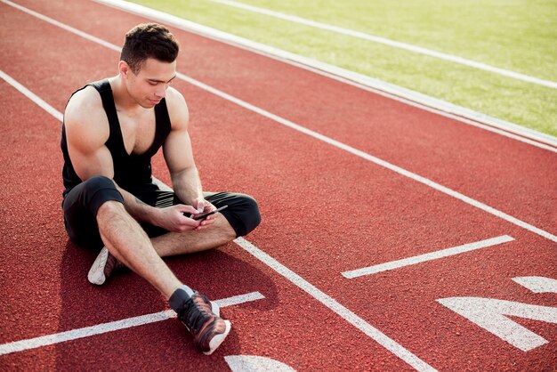 Fitness young man using mobile phone while sitting on race track