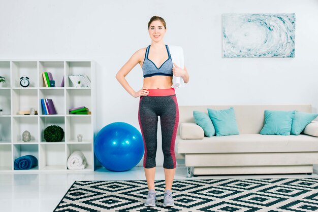 Fitness young woman holding towel over shoulder standing in the living room