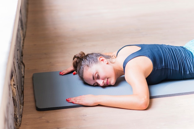 Fitness young woman lying on exercise mat over the wooden background