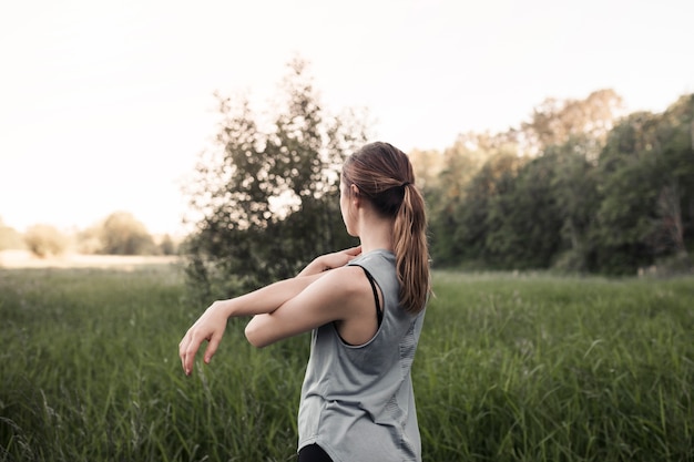 Fitness young woman stretching her hand standing in green grass