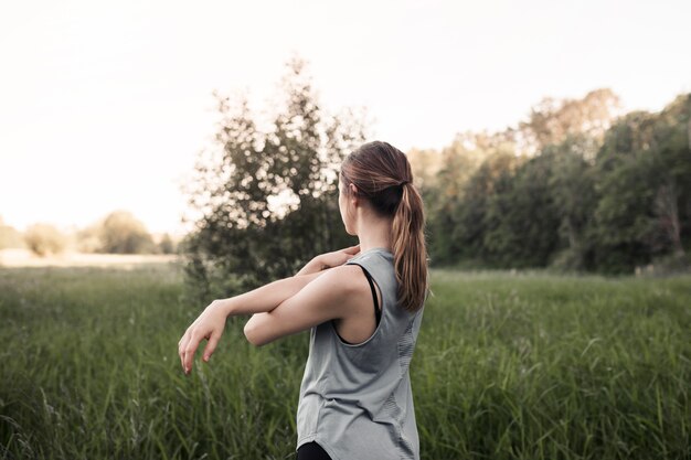 緑の草の中に立っている彼女の手を伸ばすフィットネス若い女性