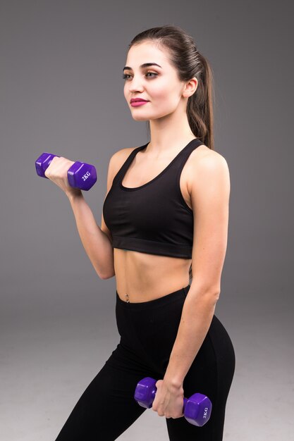 Fitness young woman with dumbbells on a gray wall. Sport lifestyle.