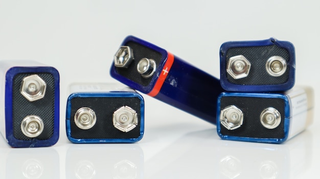 Пять синих использованных, хаотично расположенных и разбросанных батареек pp3 на белом фоне с отражением. главный аккумулятор для персональных источников питания. крупным планом - поцарапанный и использованный разъем аккумулятора. Premium Фотографии