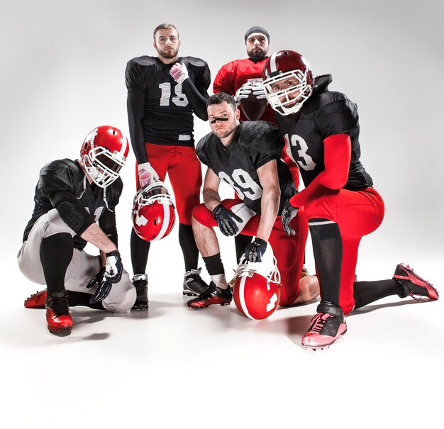 The five caucasian fitness men as american football players posing  full-length with a ball on white background