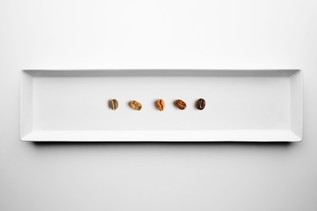 Five different grades of roasting coffee beans, aromatic, from raw to fully roasted, isolated on white plate top view