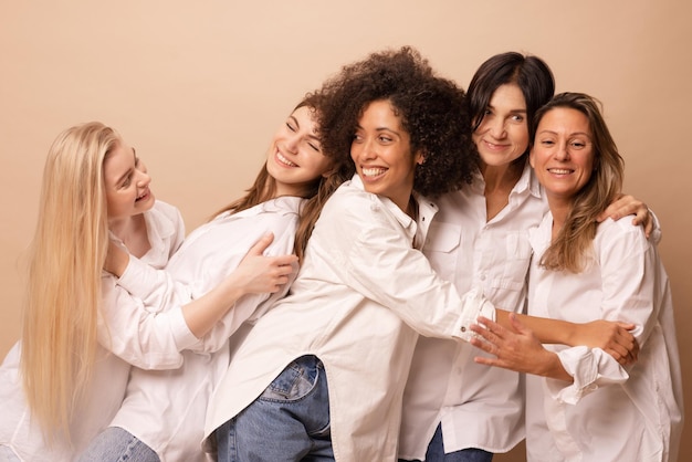 Five diverse interage women wearing white shirts and jeans are having fun against beige background Lifestyle friendship and people concept