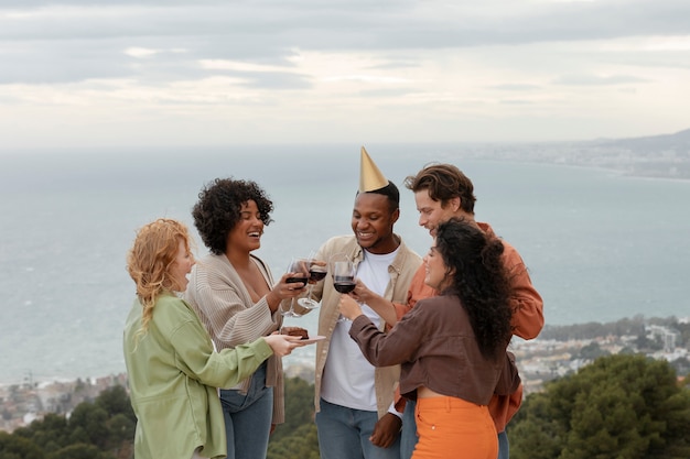 Пятеро друзей тостят с бокалами вина и улыбаются во время вечеринки на свежем воздухе