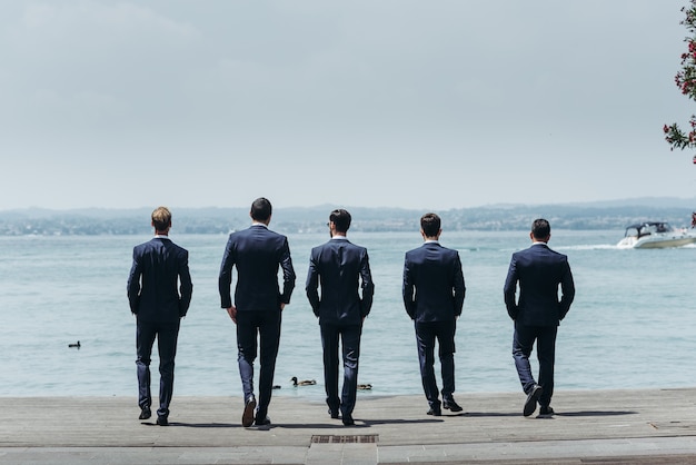 Free photo five men in classy suits walk towards the blue sea