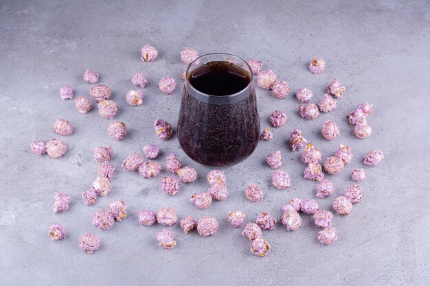 Free photo fizzy glass of cola in the middle of scattered popcorn candy on marble background. high quality photo