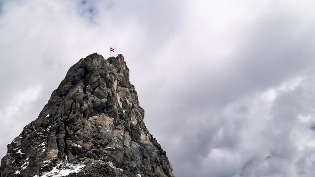 Flag of Latvia on top of a rocky mountain under a cloudy sky