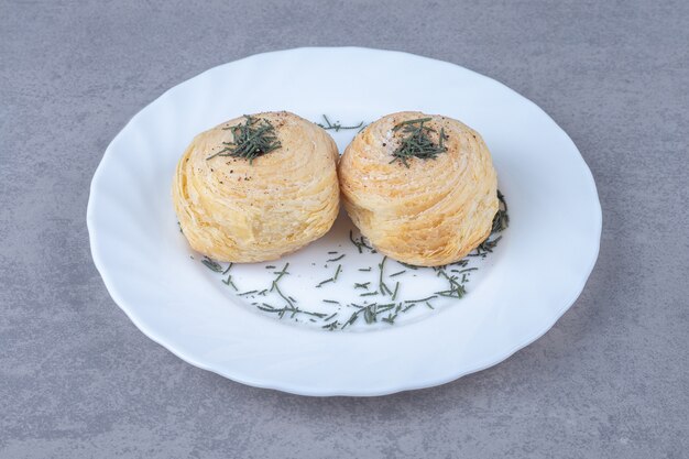 Flaky cakes on a platter decorated with pine leaves on marble table.