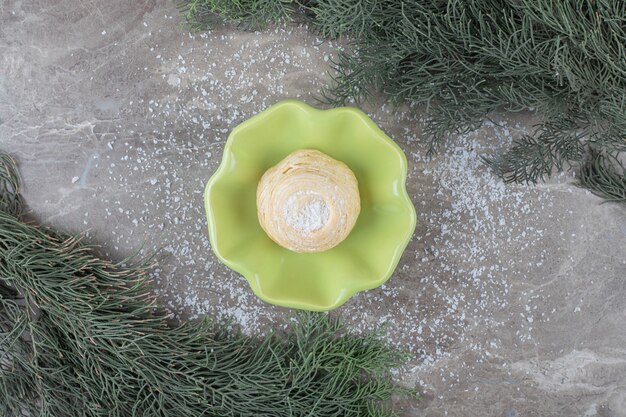 Flaky cookie in a small bowl between pine branches on marble surface