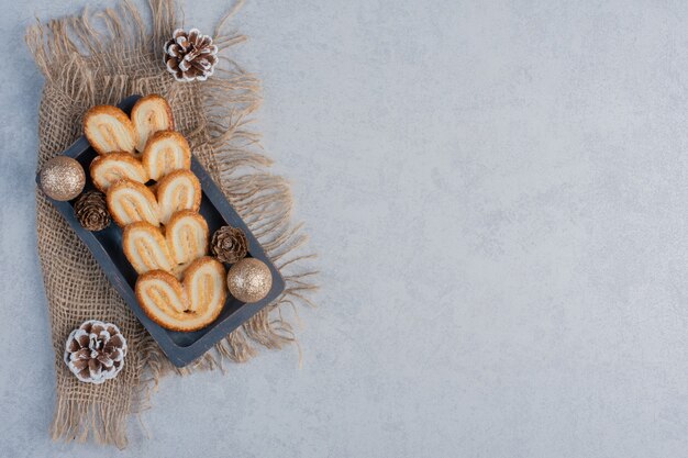 Flaky cookies and christmas adornments on a small tray on marble surface