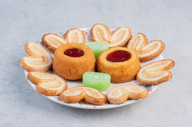 Flaky cookies, marmelades and jelly-filled cakes on a platter on marble table.