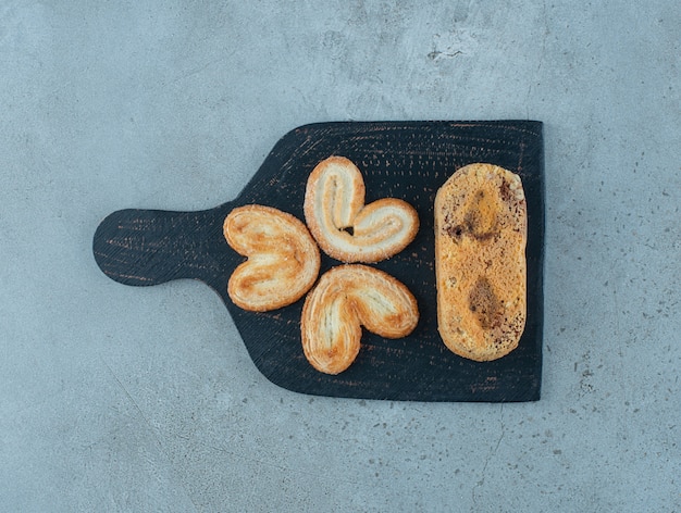 Flaky cookies and a small cake on a board on marble background. High quality photo