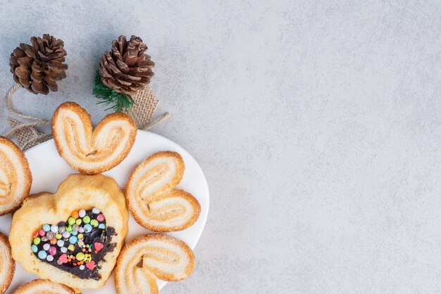 Flaky cookies and a small cake on a platter next to pine cones on marble table.